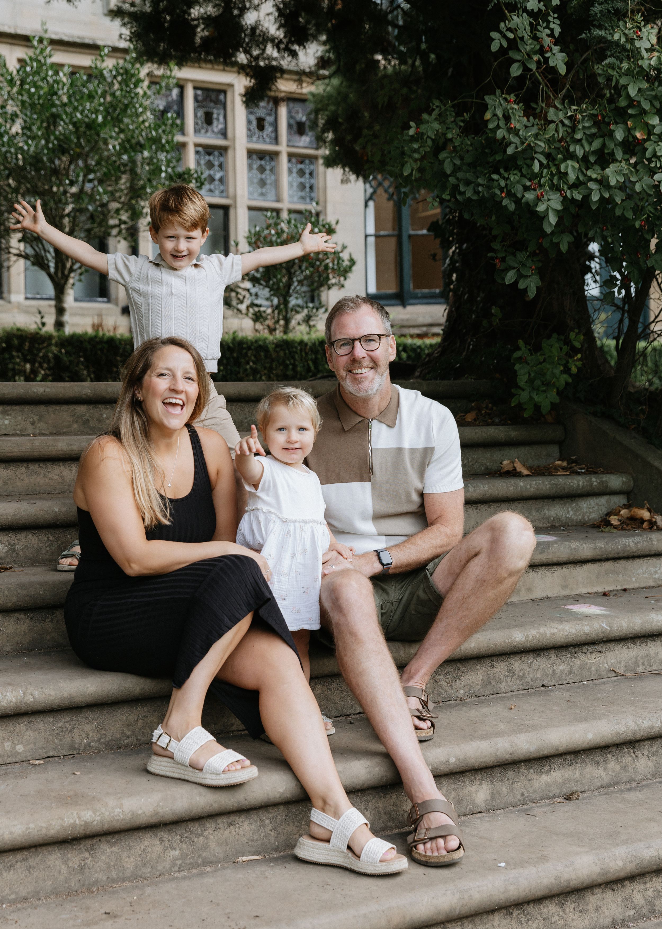 A family sits together on outdoor stone steps while sharing joyful moments and laughter on a sunny day.
