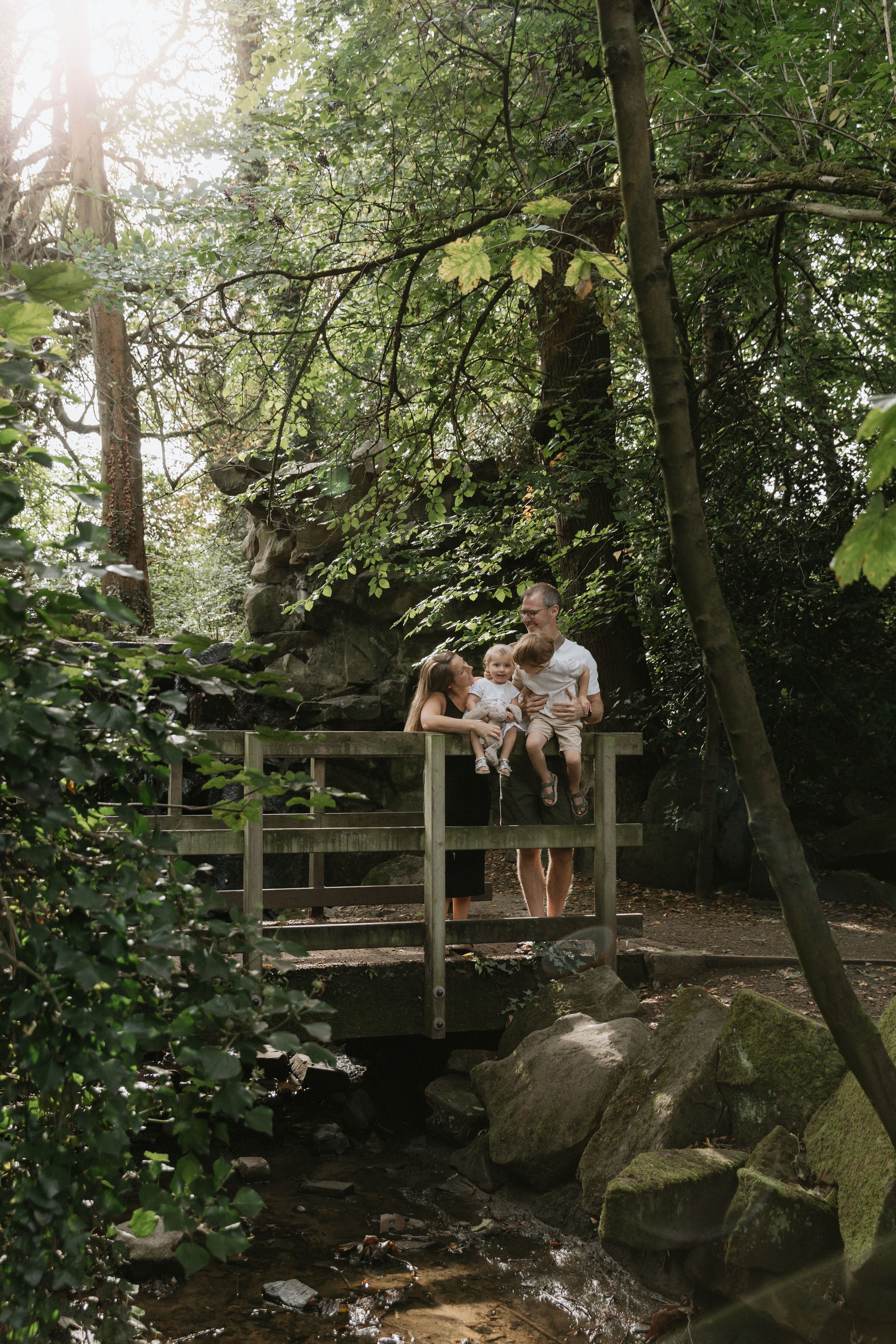 People relaxing on a wooden deck platform surrounded by lush forest and large boulders near a stream.