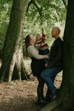 A playful family photo session in a wooded forest setting with natural lighting and tree trunks in the background.