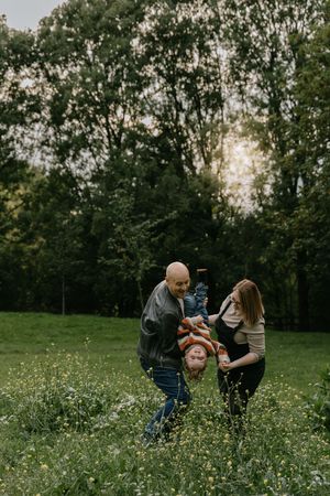 Family members playing together in a grassy field surrounded by trees during a golden hour photo session.