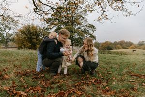 Family enjoying a cozy autumn photoshoot together on a grassy hill surrounded by fallen leaves.