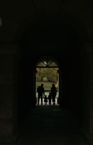 Dark silhouettes of people standing in an archway entrance against a backlit background.