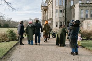 People gather outside a historic stone manor house on a cloudy winter day.