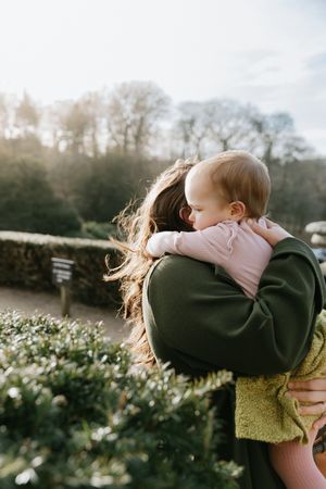 A parent lifts and spins a child in the air against a sunlit background with wildflowers.