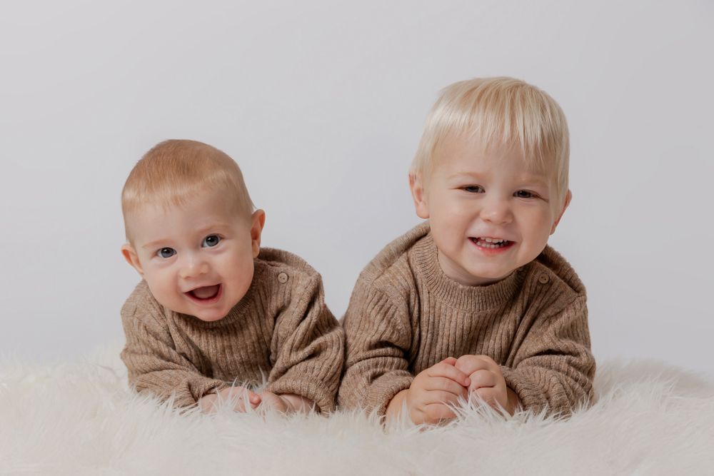 Studiefoto af babyer iført matchende beige trøjer, liggende på hvidt pelsunderlag. Børnefotograf Fyn