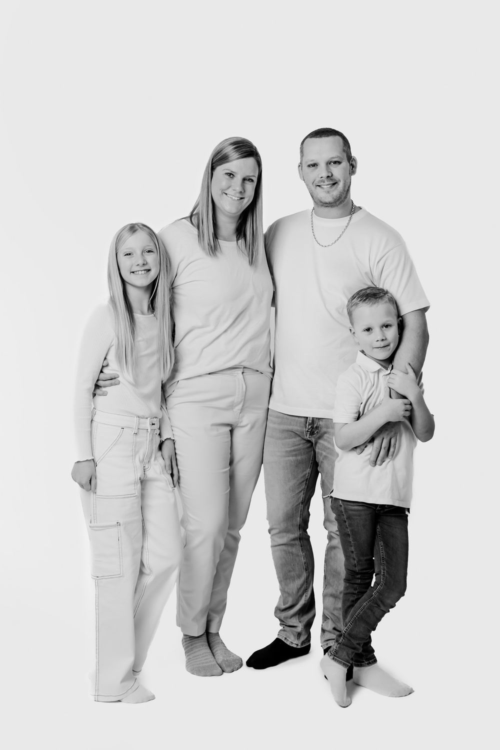 Familiegruppeportræt i afslappede hvide outfits foran lys baggrund. Børnefotograf Fyn