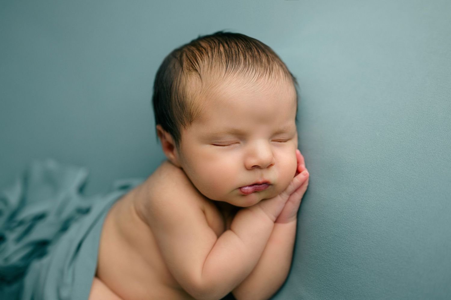 Peaceful sleeping newborn baby wearing delicate pink feathered headband against soft mauve background.
