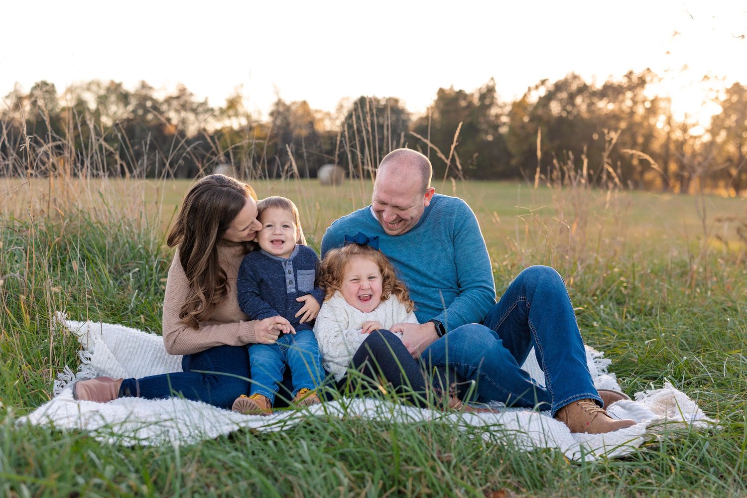 Family shares laughter while relaxing on picnic blanket in sunny field.