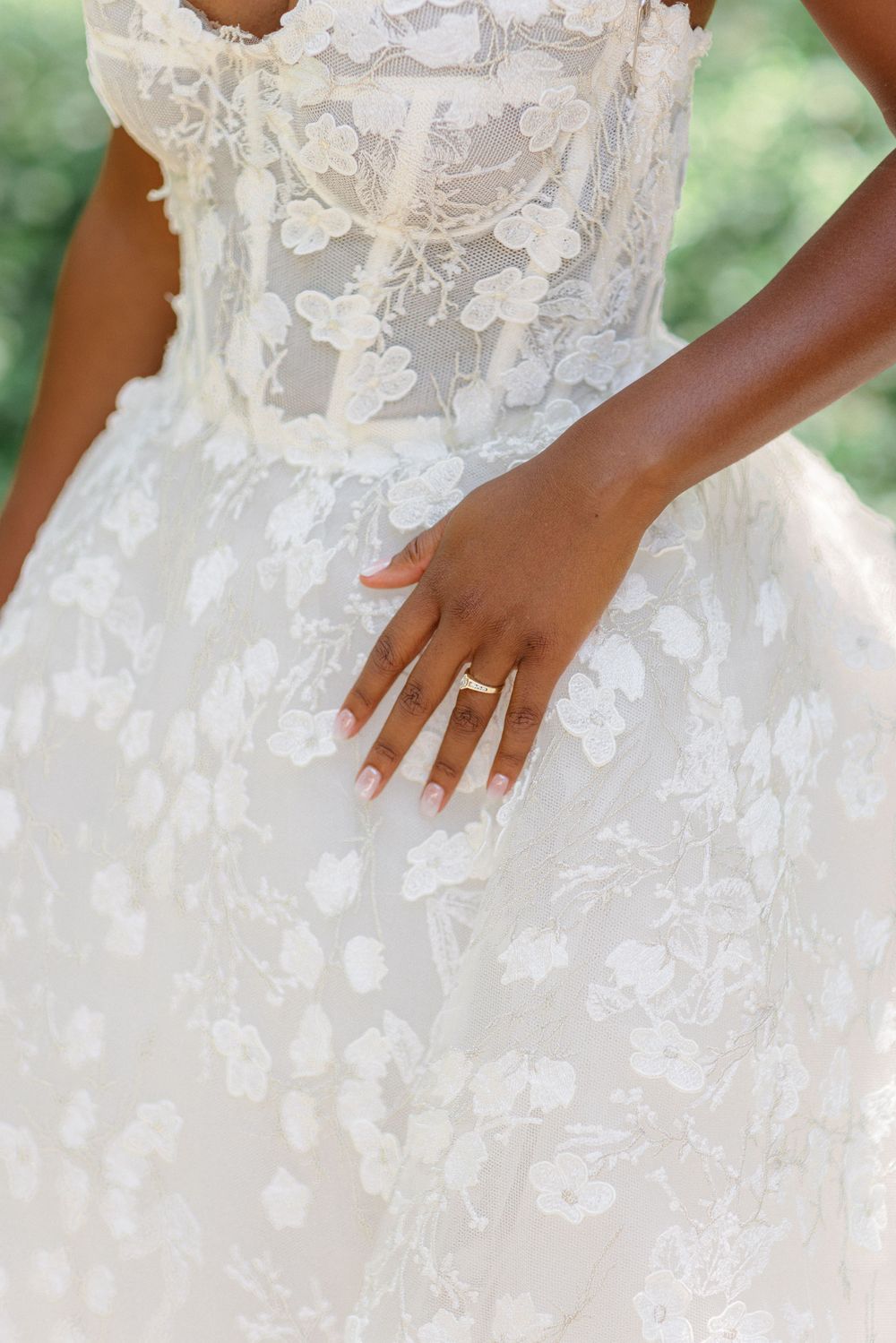 Close-up of a detailed white lace wedding dress with an elegant engagement ring on display.