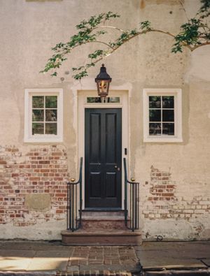 Classic Charleston doorway with black door, white trim, and brick detailing beneath hanging lantern.