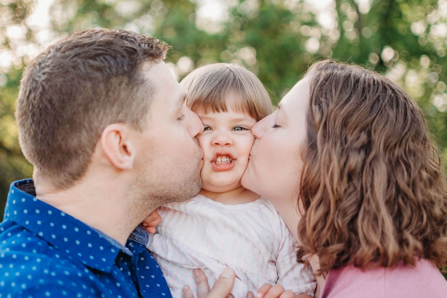 A sweet family photo shows affectionate moment outdoors in natural lighting.