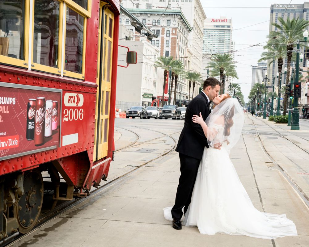 A romantic wedding photo with a couple kissing next to a red streetcar in New Orleans.