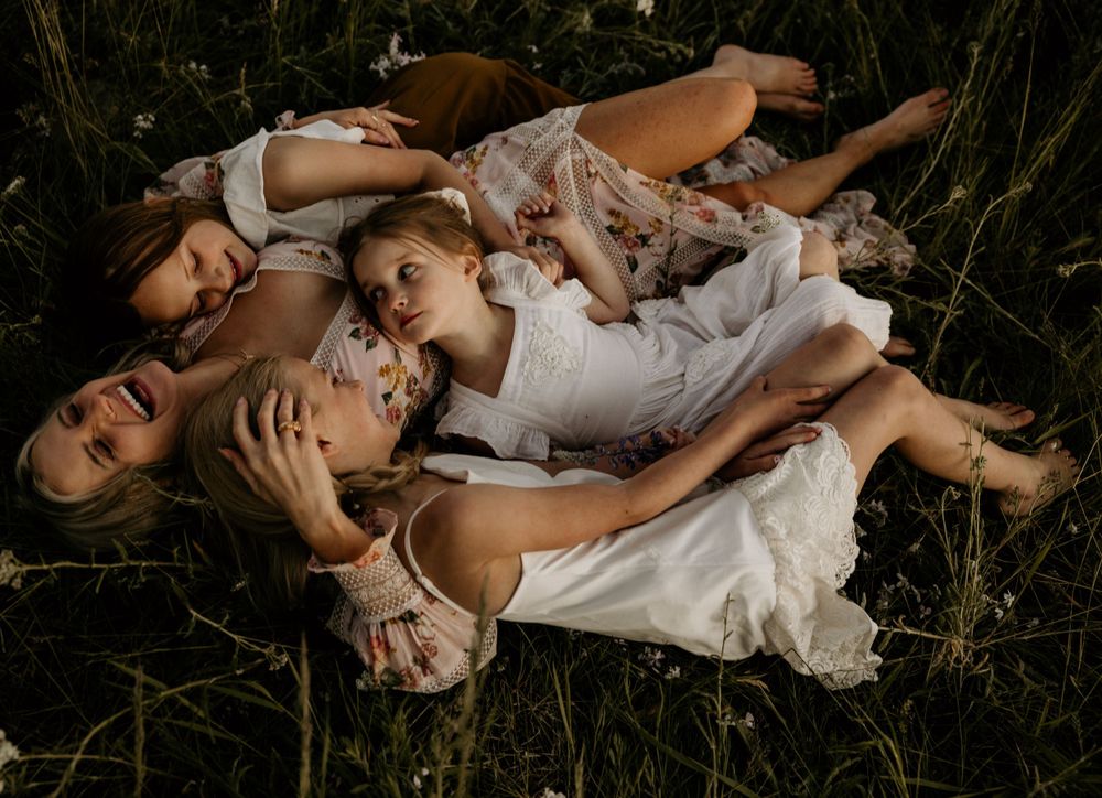 A joyful mother curled up with her little girls, laughing and playing in sunny grassy field