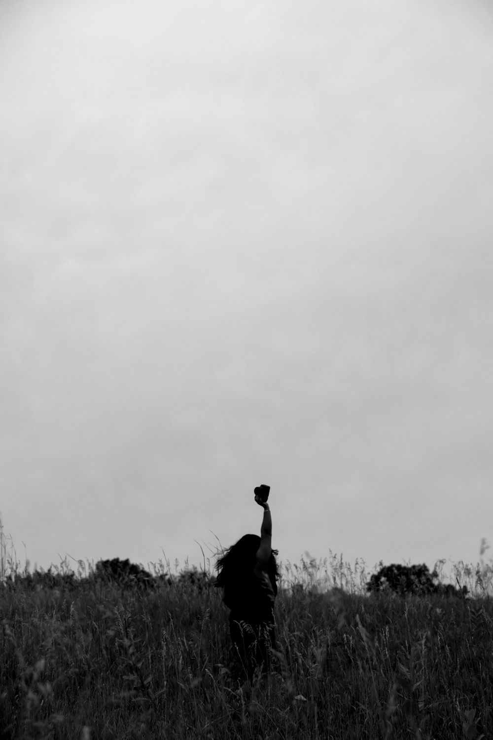 Silhouette of person standing on hilltop against gray sky in black and white.