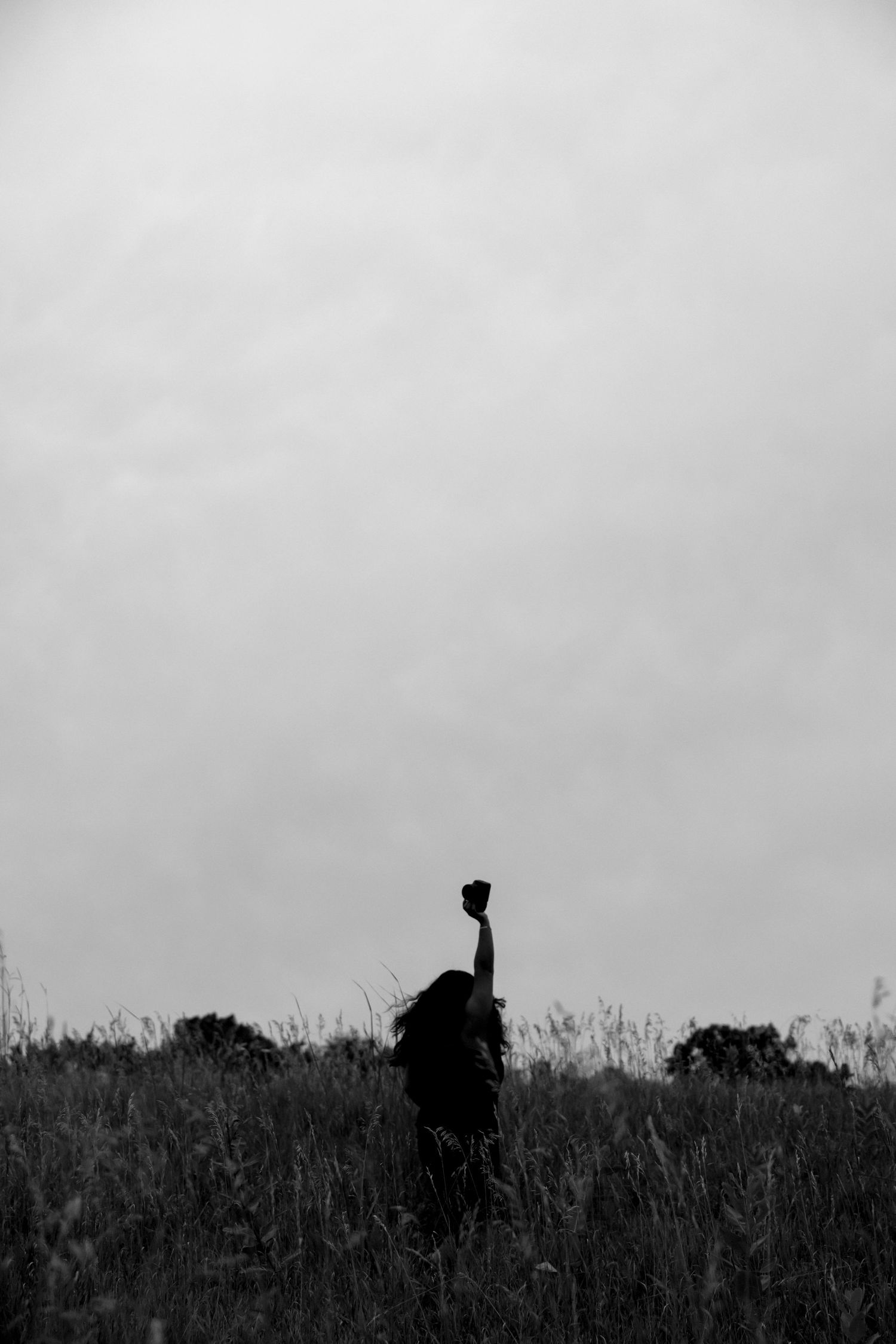 Silhouette of person standing on hilltop against gray sky in black and white.