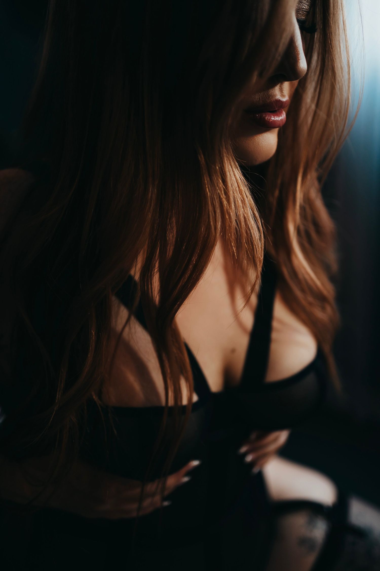 Woman in black lingerie, holding her straps while gazing into the camera, captured in soft, intimate lighting.