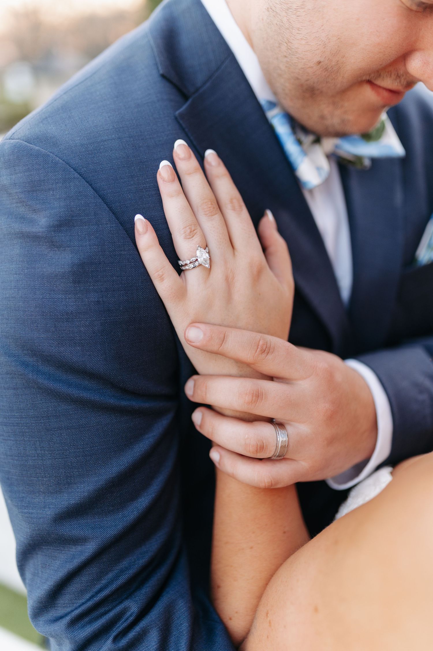 Close-up of bride and groom hands showing diamond engagement ring and wedding band at wedding ceremony.