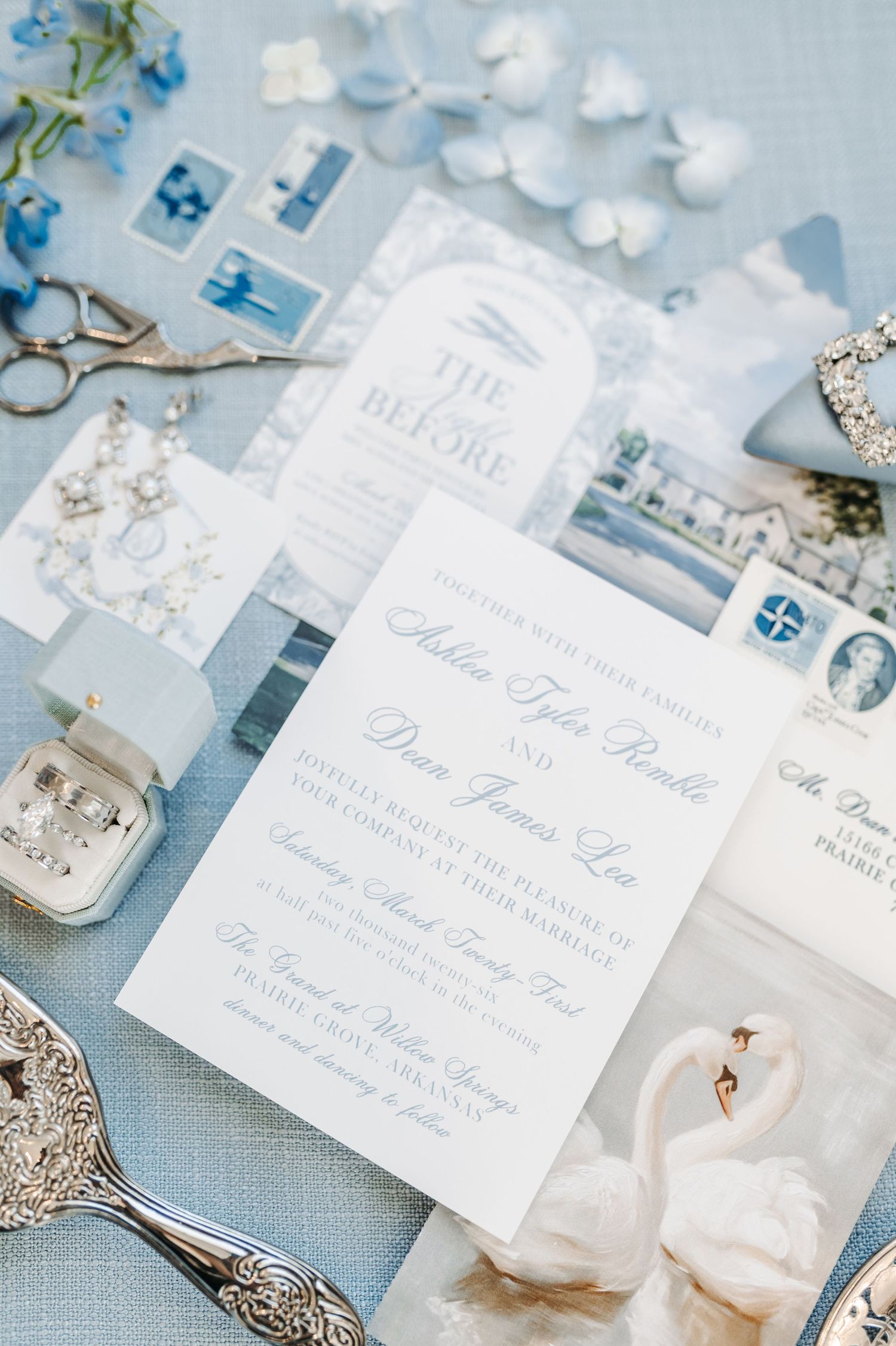 Elegant blue and white wedding invitation suite with swan details, jewelry, scissors, and floral accents on a soft blue background.