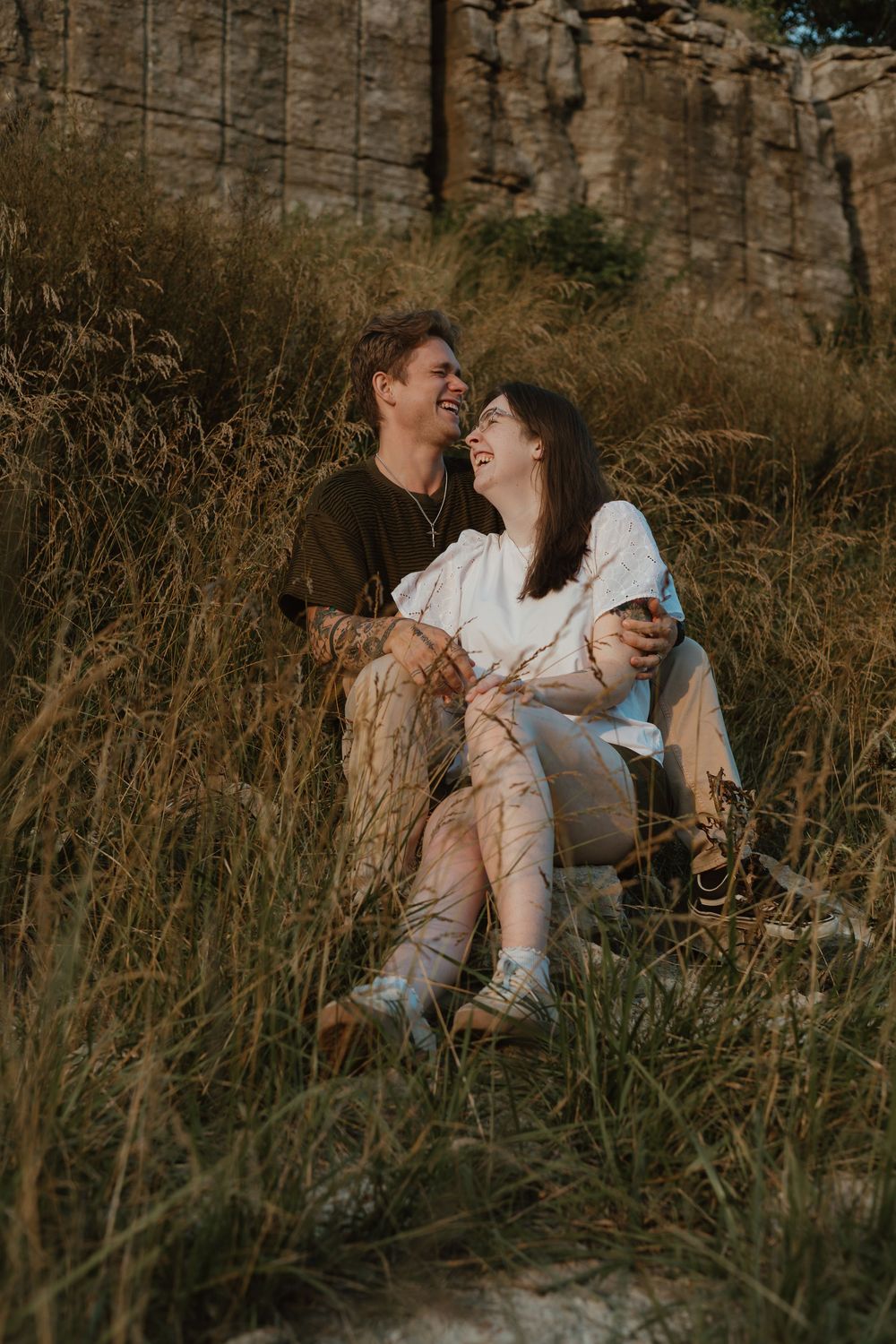 A couple shares tender moments while sitting in tall grass during golden hour in a romantic outdoor photoshoot.