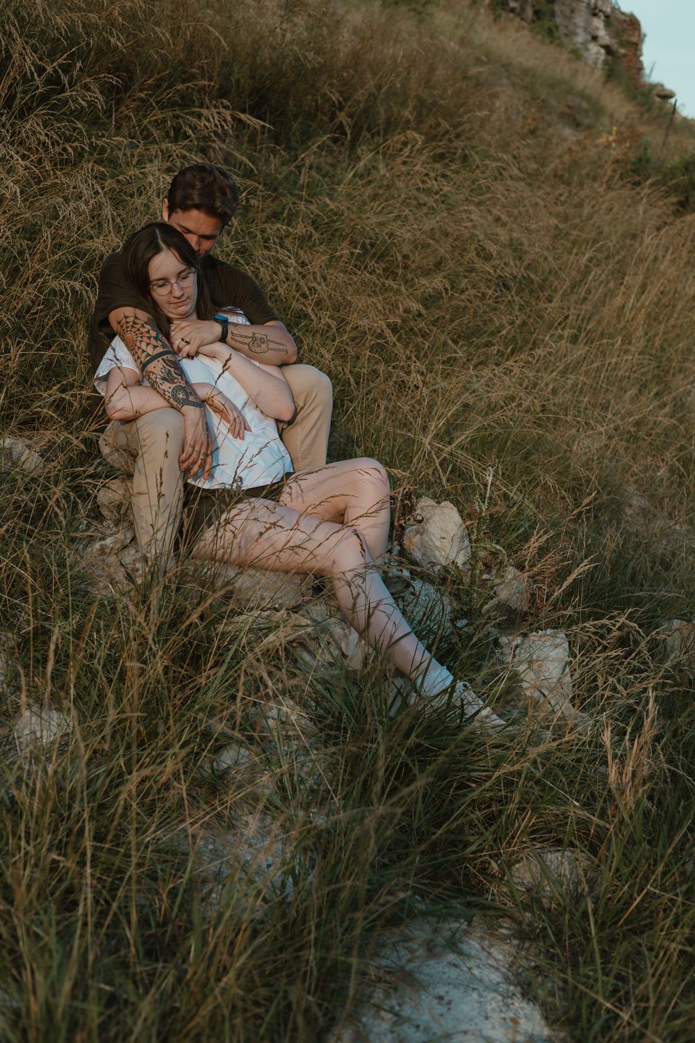 A couple shares intimate moments while lying in tall grass during a sunset photography session.