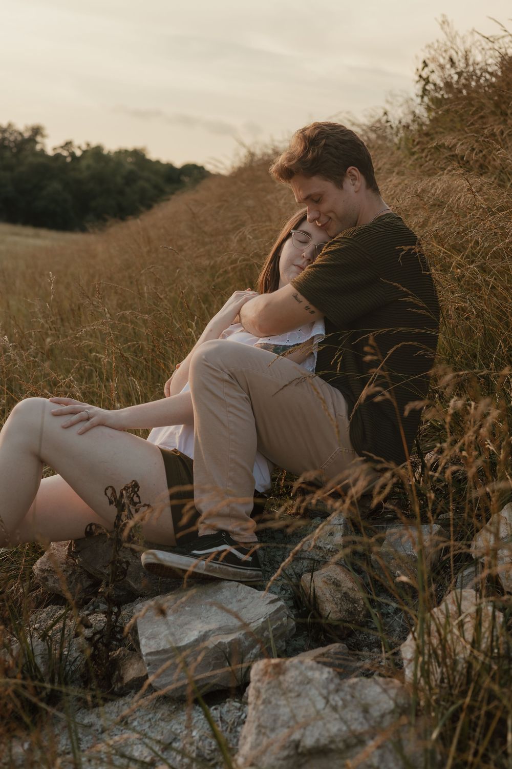 A romantic couple lounges together in a sunlit meadow during golden hour, creating an intimate outdoor portrait series.