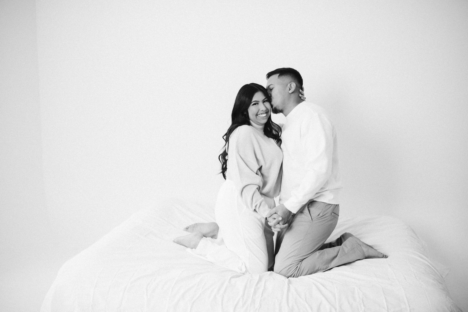 Intimate black and white portrait of couple embracing on white bedding.