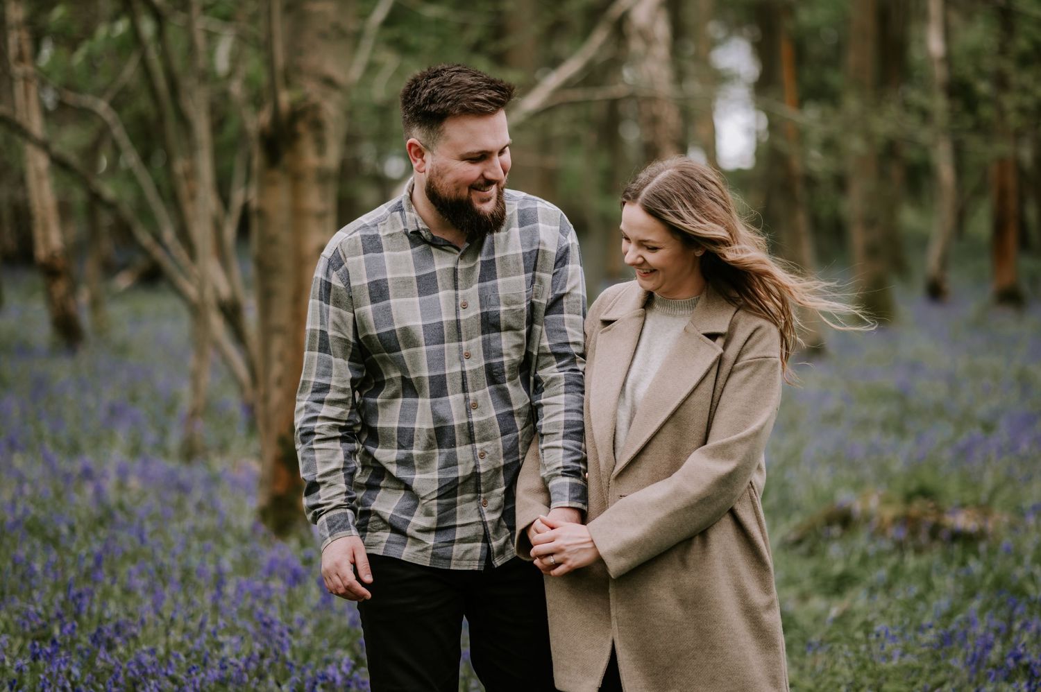 Happy couple walking through bluebells in springtime woodland.