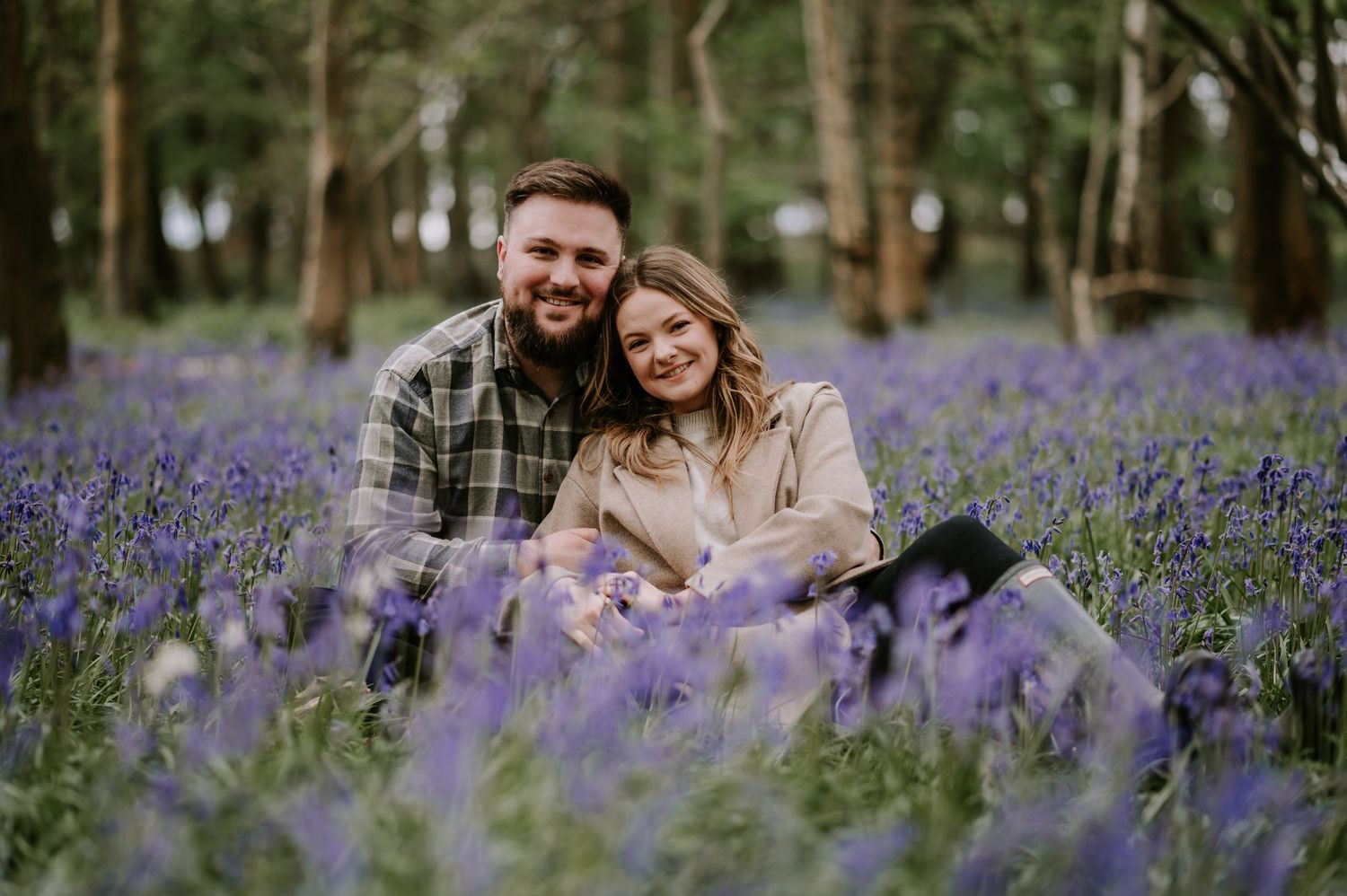 Couple sitting among purple bluebells in enchanted forest setting.