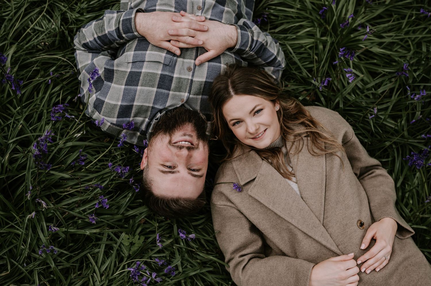 Couple lying in field of purple wildflowers sharing intimate moment.