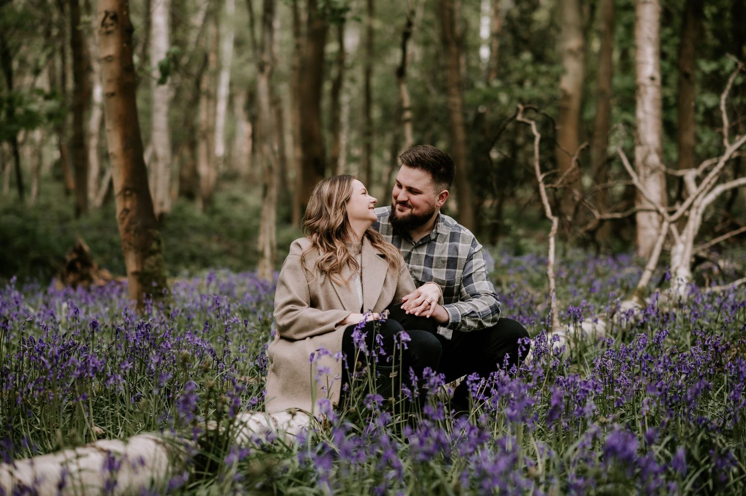 Couple sharing tender moment among purple wildflowers in woodland setting.