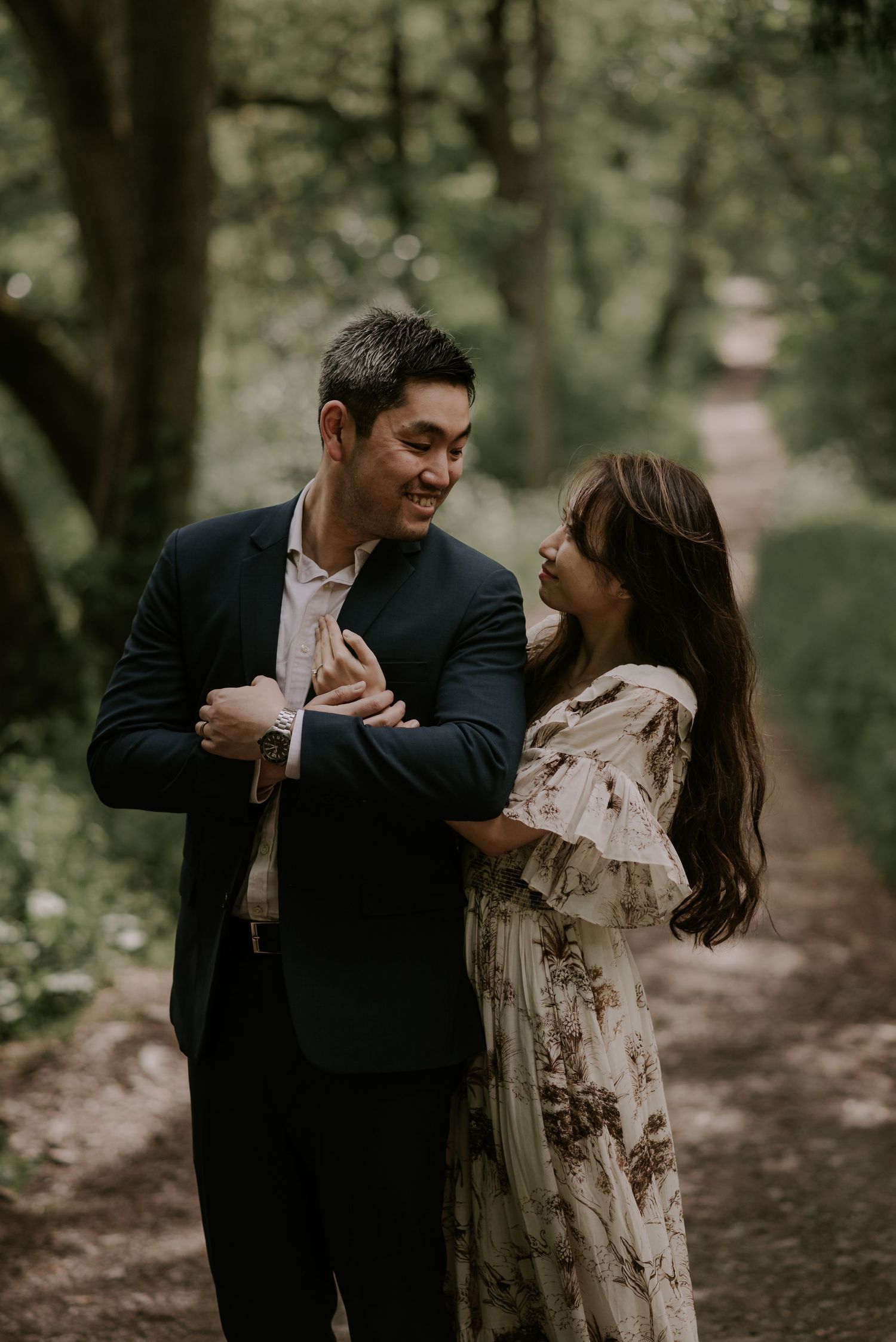 A joyful couple sharing a candid moment on a wooded path during their engagement photoshoot.