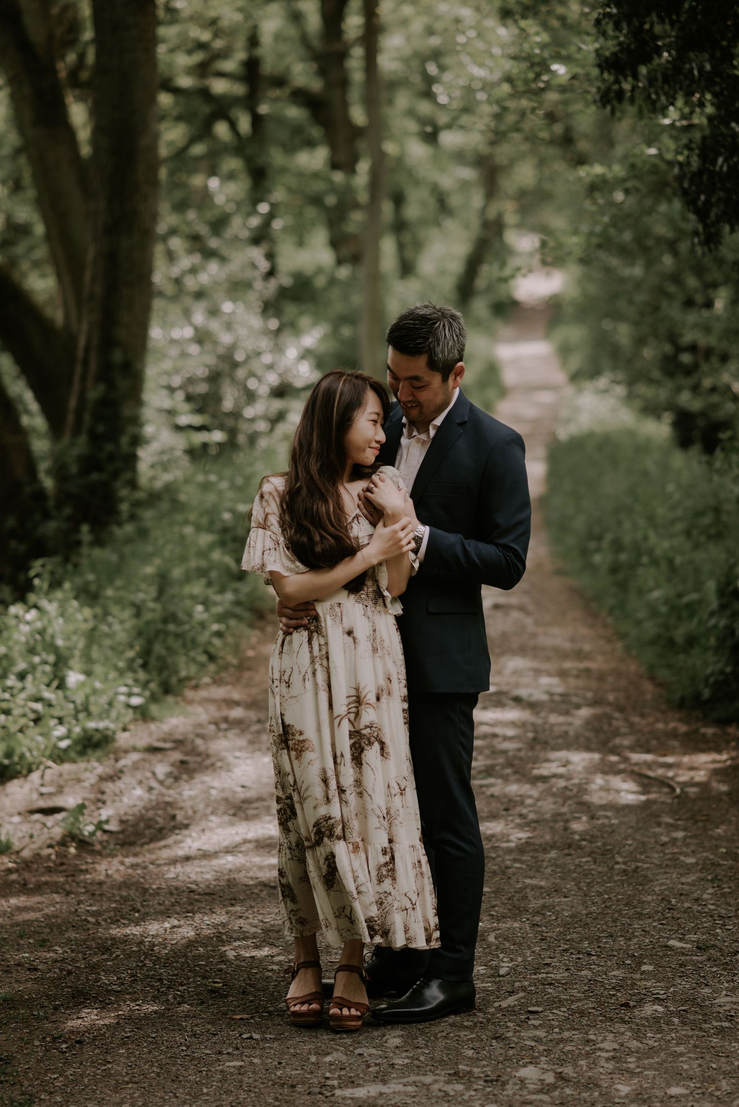 Intimate couple shares tender moments along a tree-lined forest path.