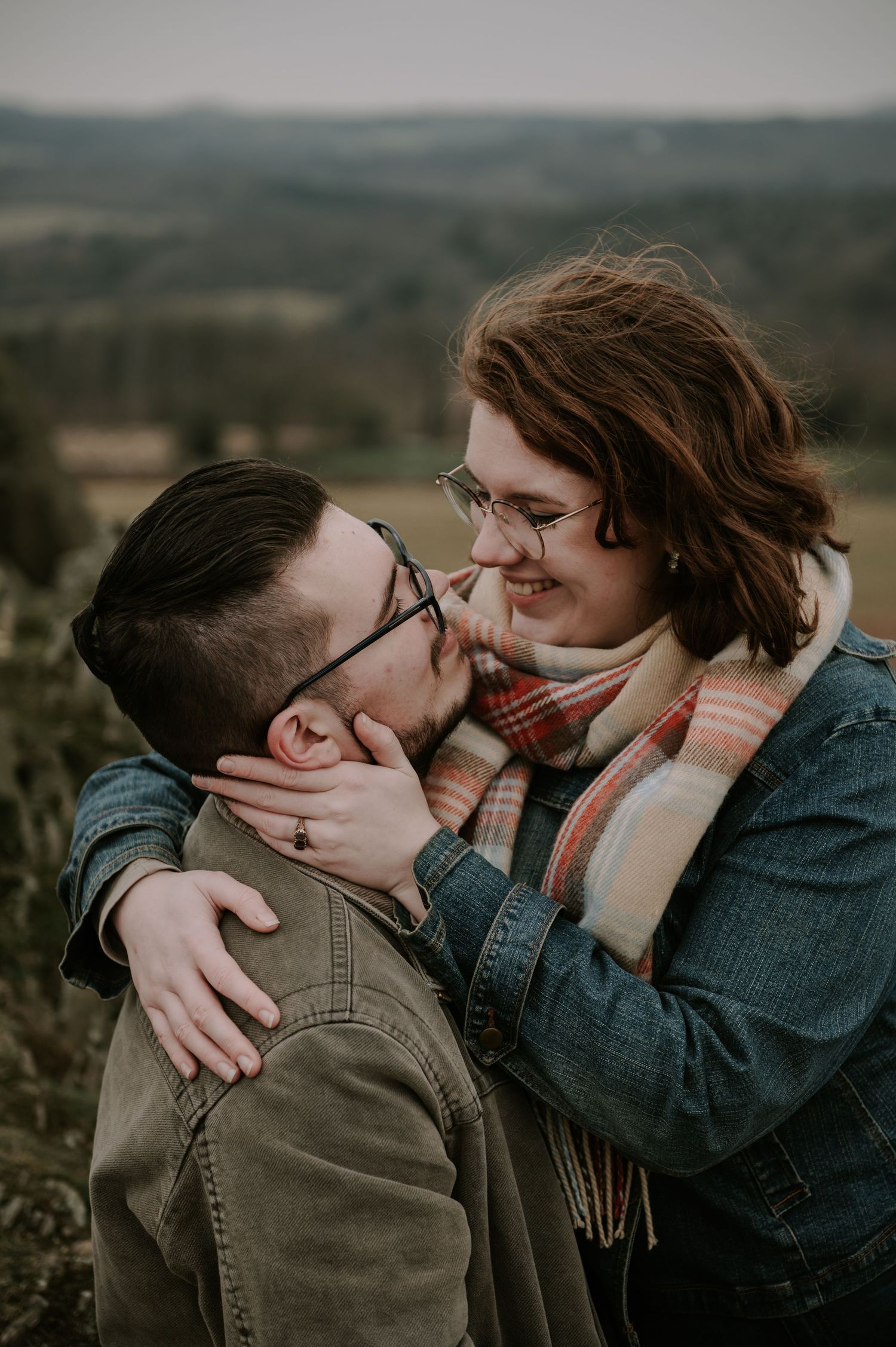 A couple shares an intimate embrace against a backdrop of rolling hills at sunset.