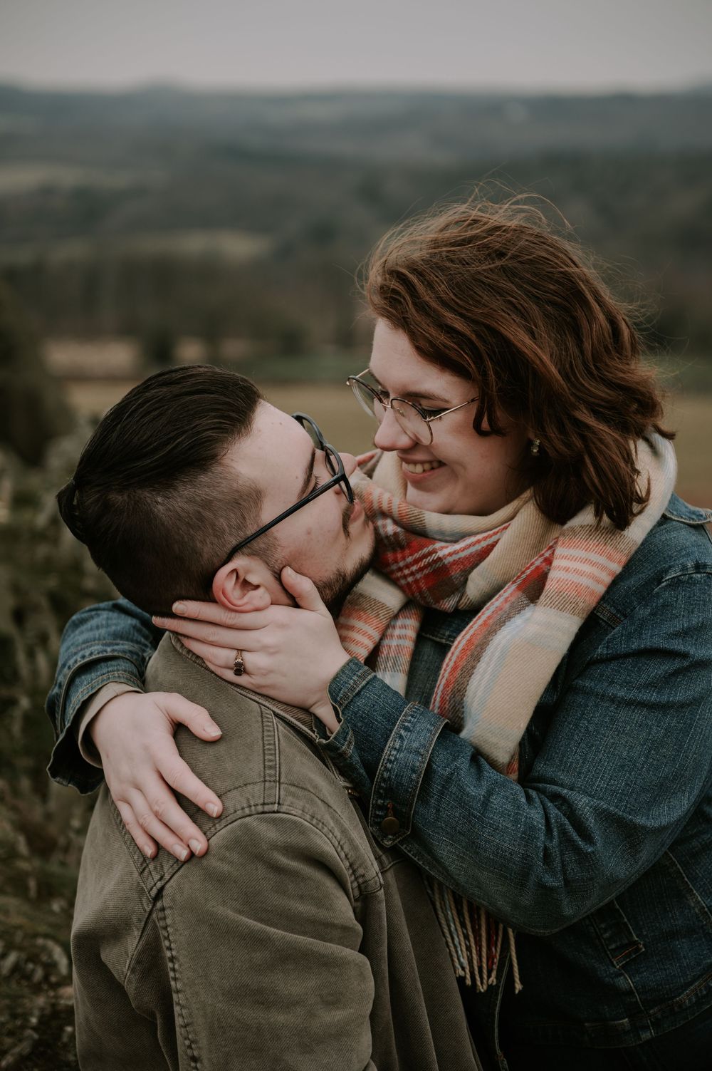 A couple shares an intimate embrace against a backdrop of rolling hills at sunset.