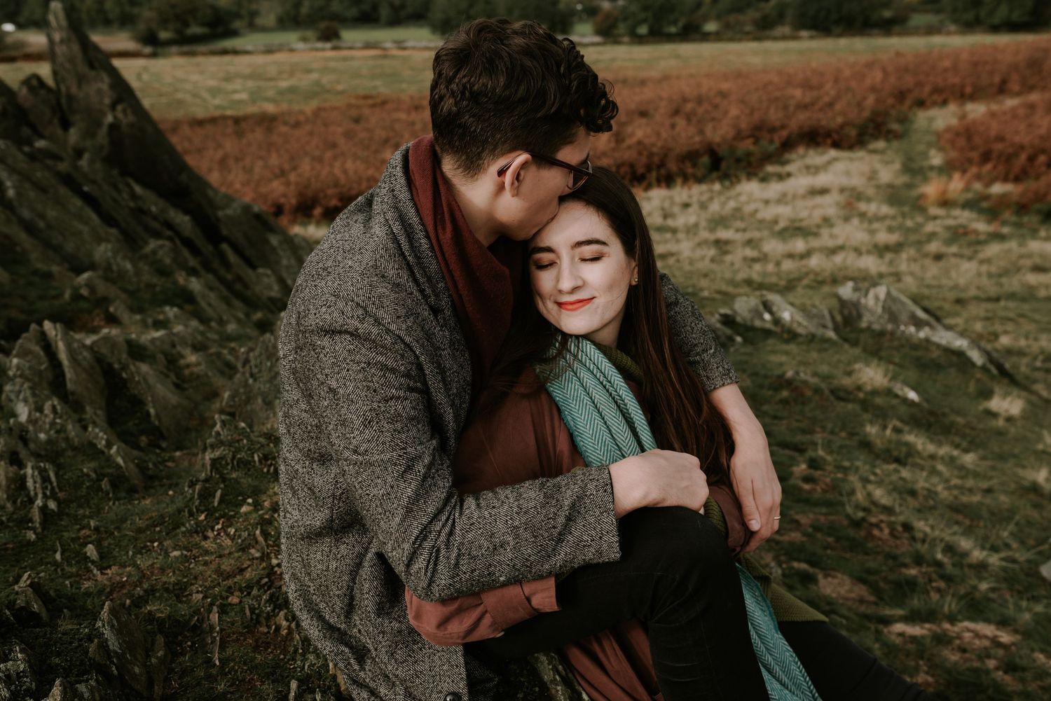 An embracing couple shares an intimate moment outdoors against a rustic autumn landscape at sunset.