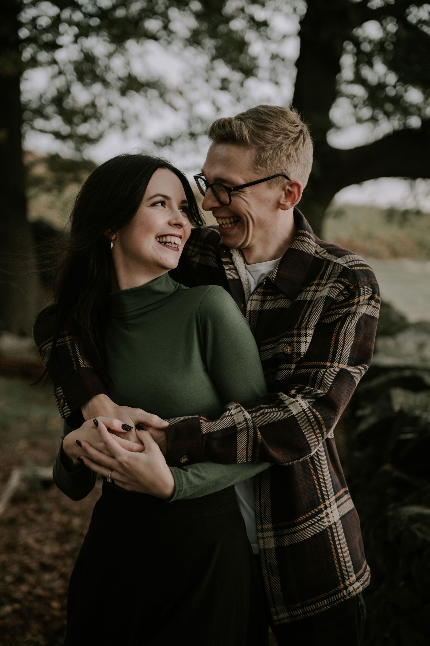 A romantic couple embraces in a forest setting with autumn bokeh lighting.