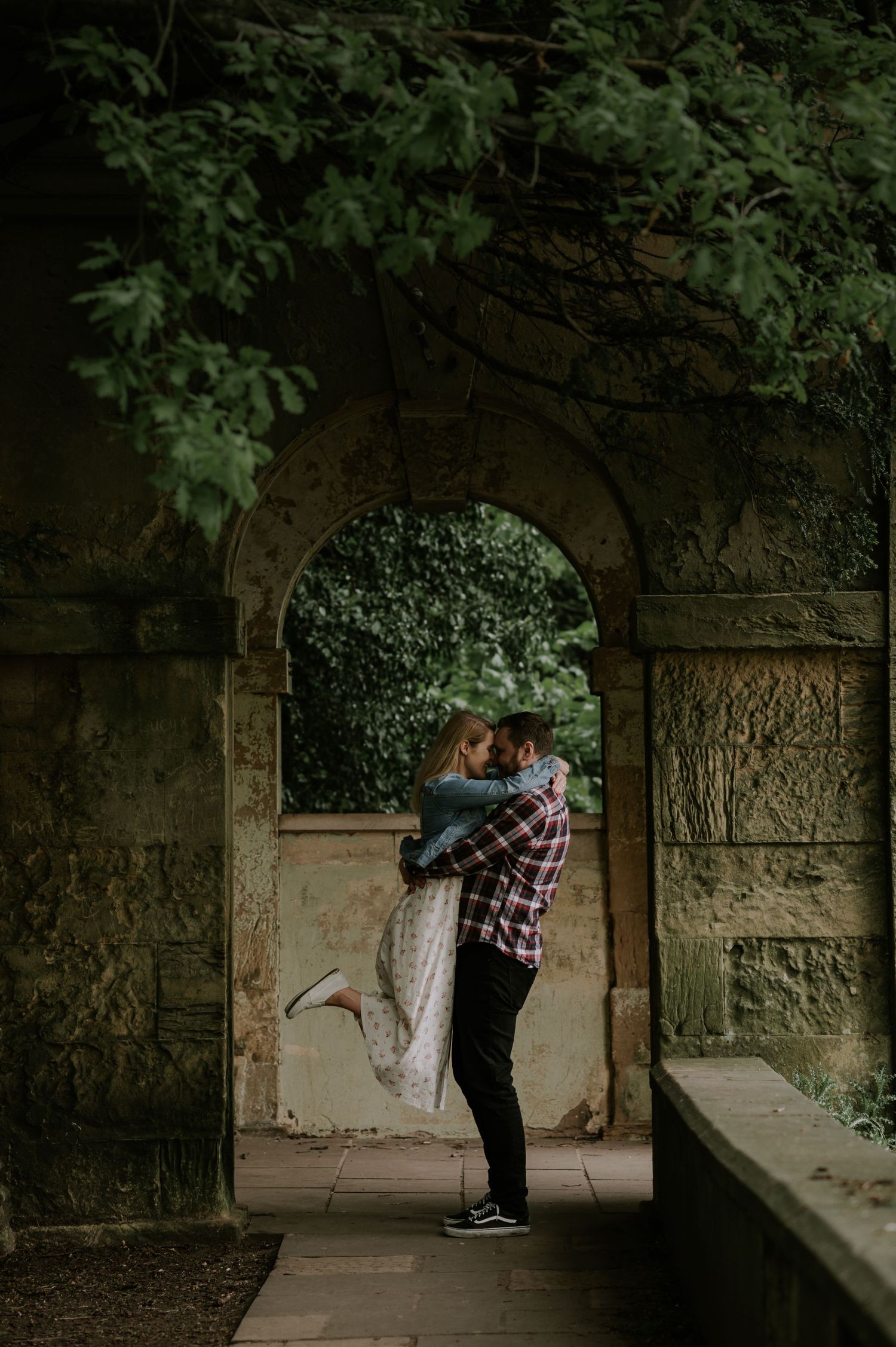 A romantic moment captured under a stone archway surrounded by lush greenery and foliage.