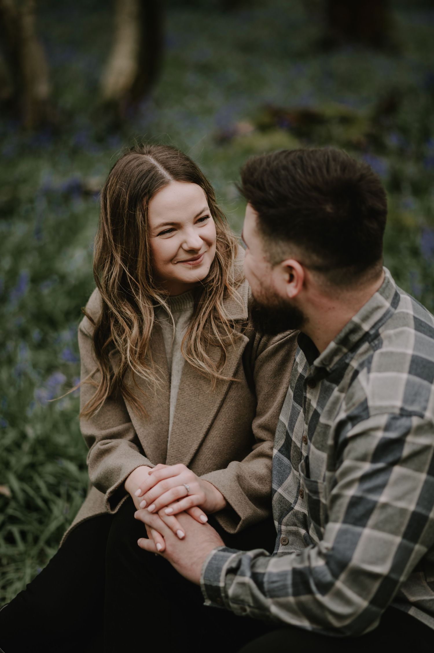 A couple shares a tender moment while sitting together among blooming bluebells in a garden setting.