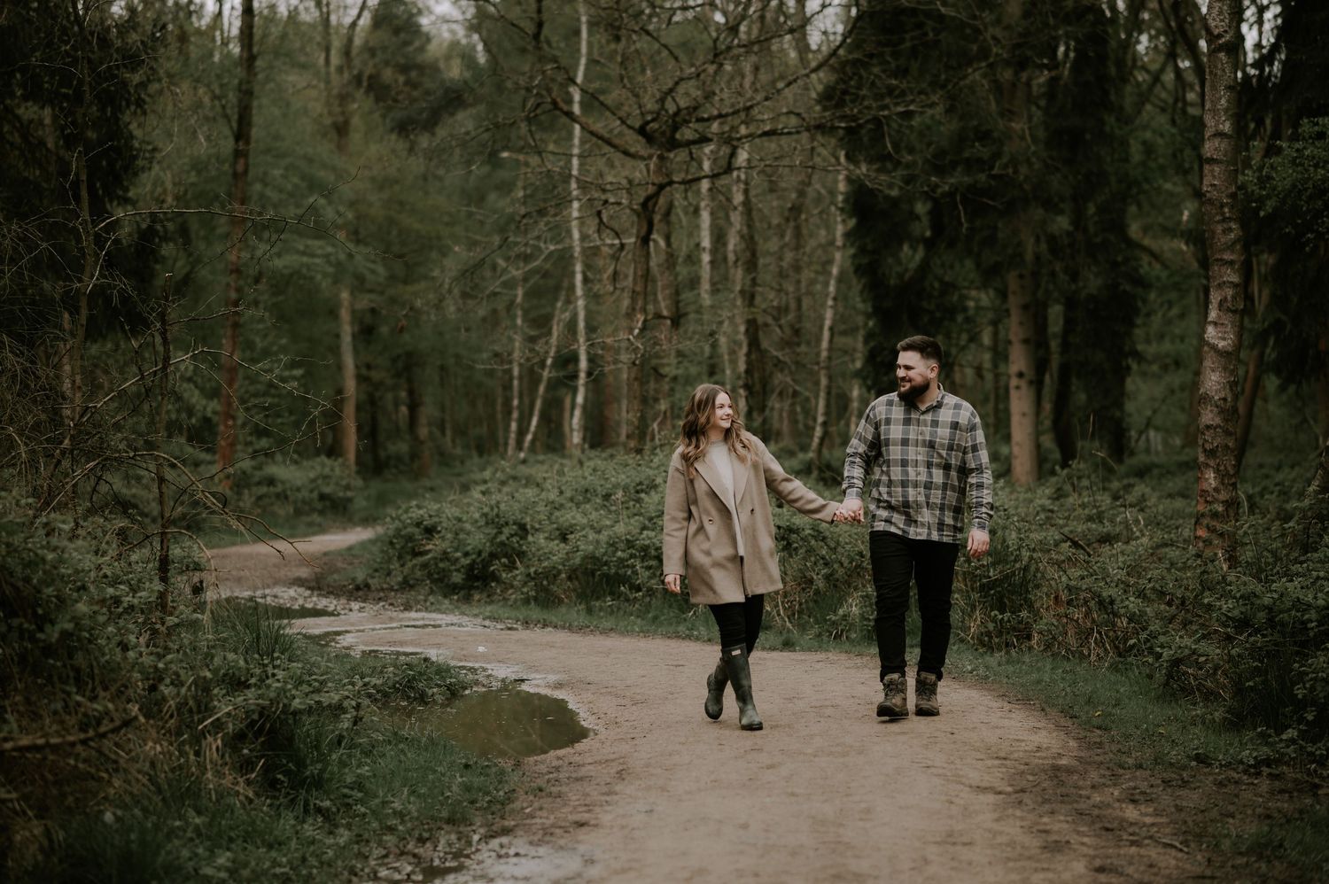 A couple walks together on a winding forest path during an outdoor photography session.