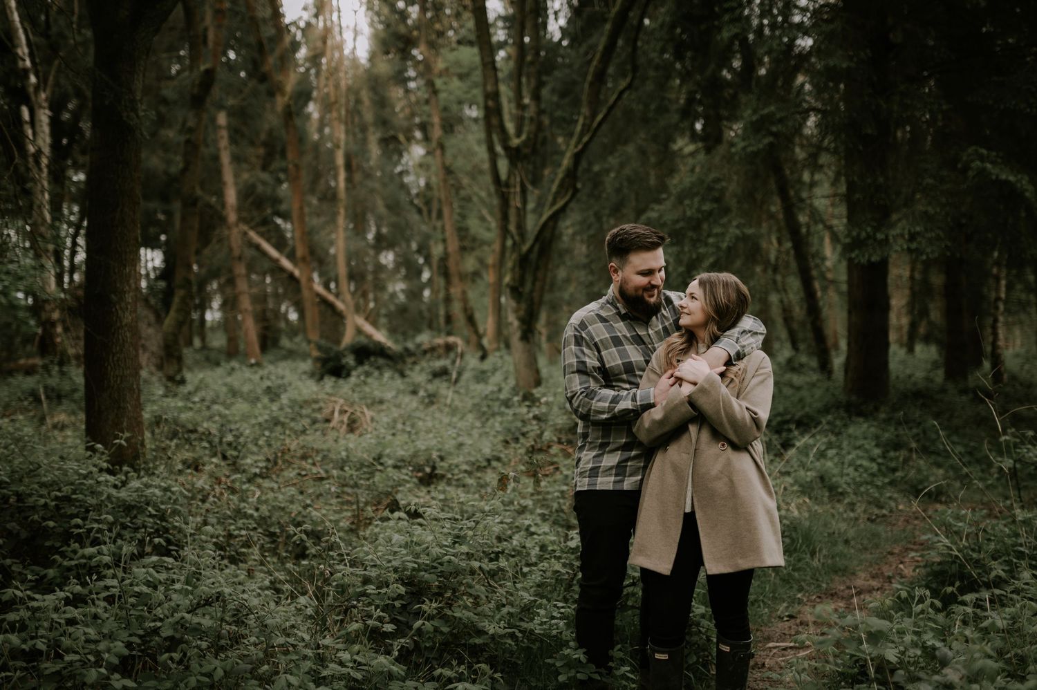 A couple shares an intimate moment while standing on a wooded trail.