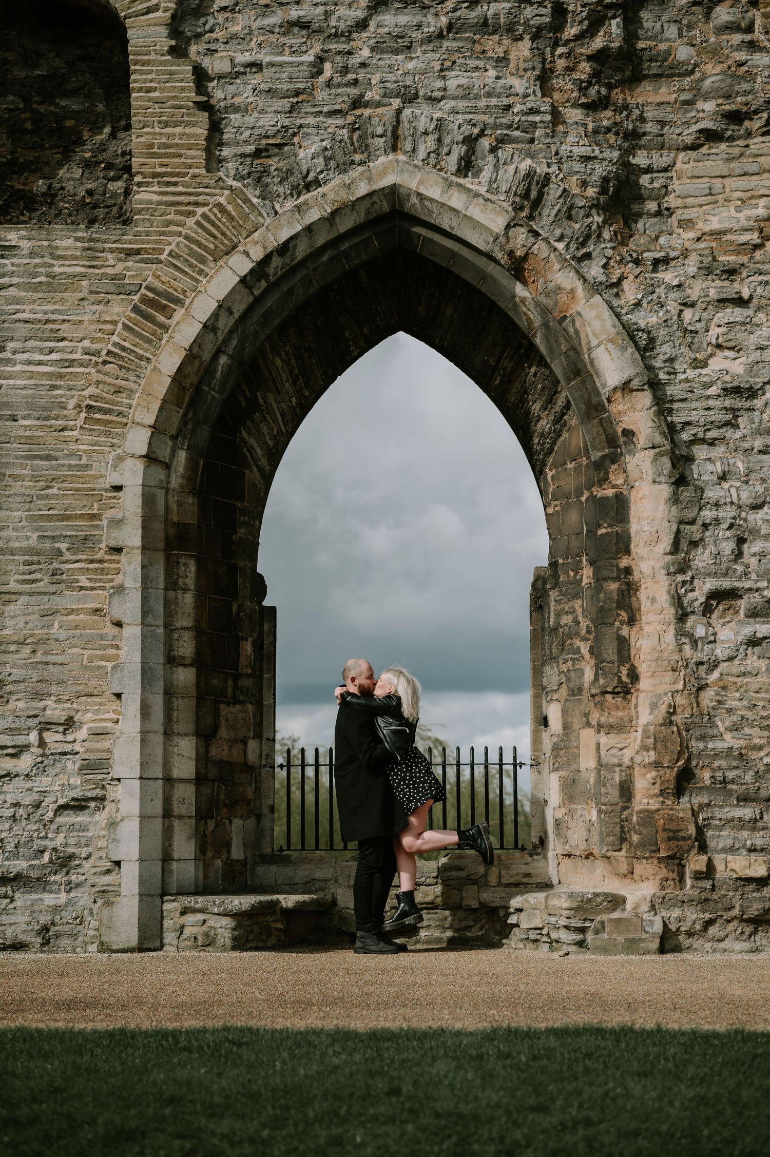 A romantic moment captured under a gothic stone archway against a moody sky.