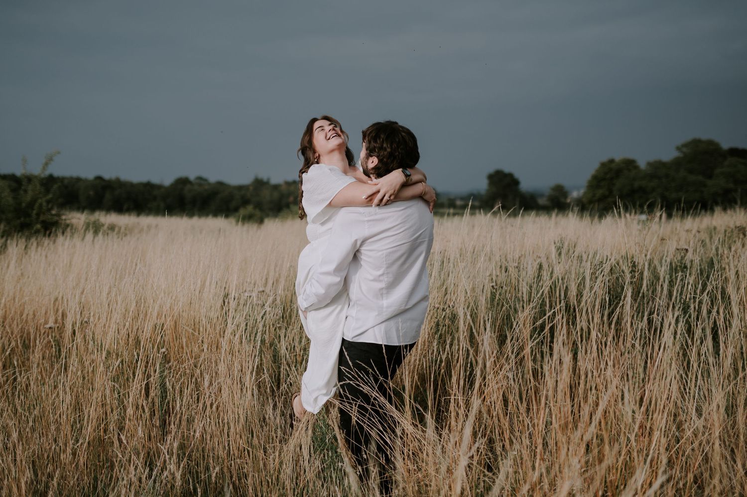A tender embrace captured in a golden field of tall grass under an overcast sky.