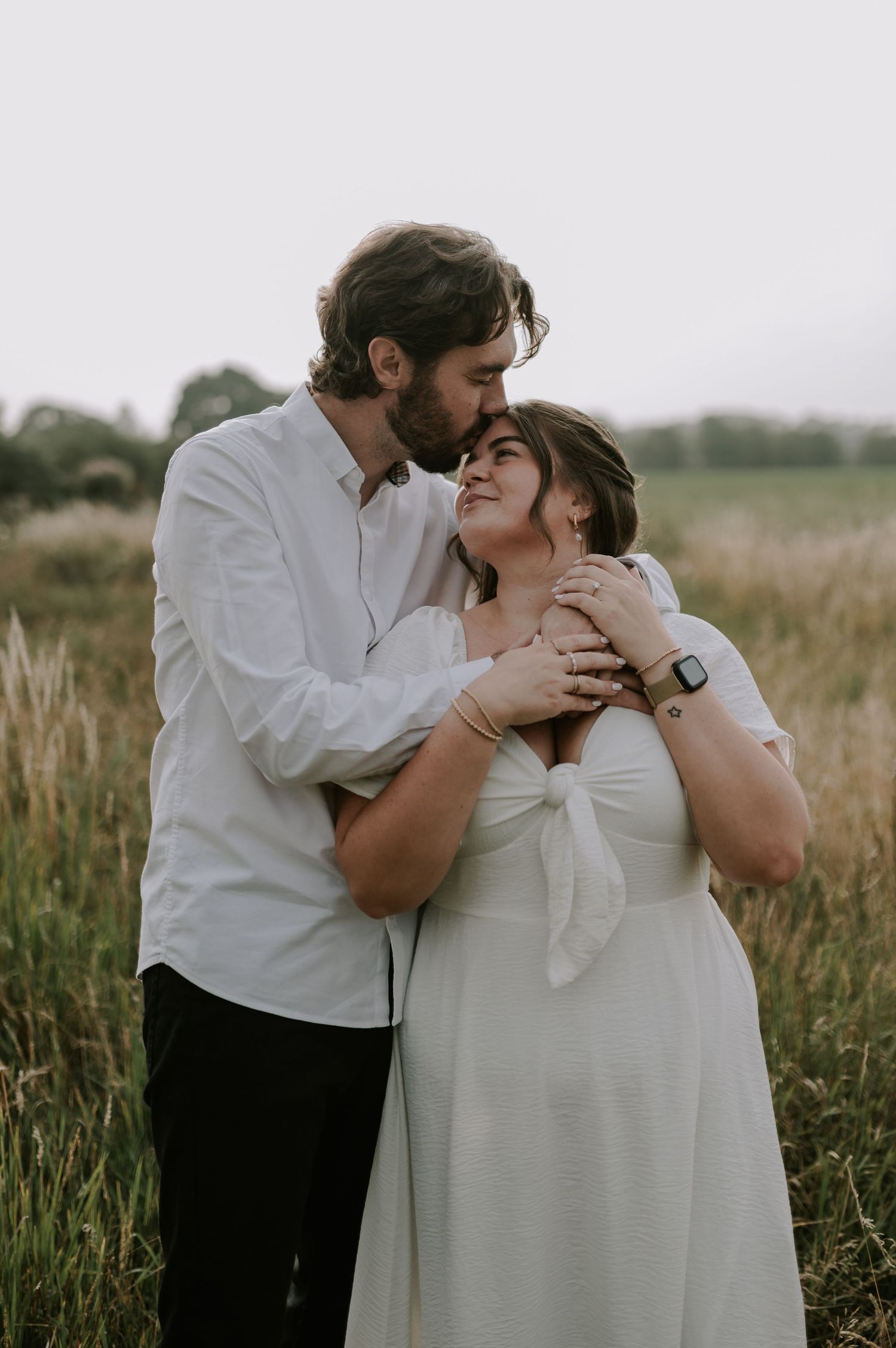 An intimate embrace between a couple standing in a scenic field at sunset.