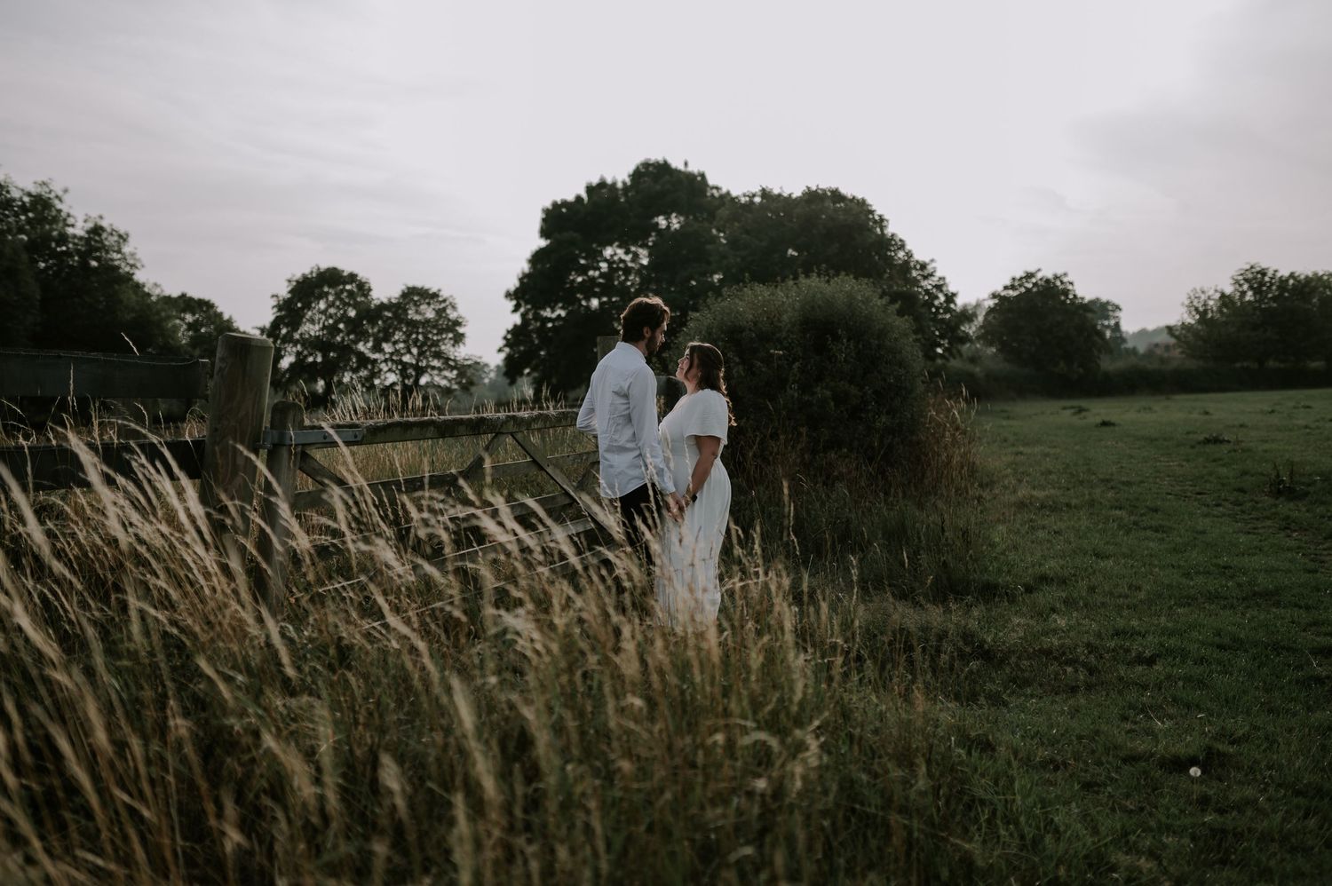 Silhouetted figures walking together in misty field with tall grass at sunset.