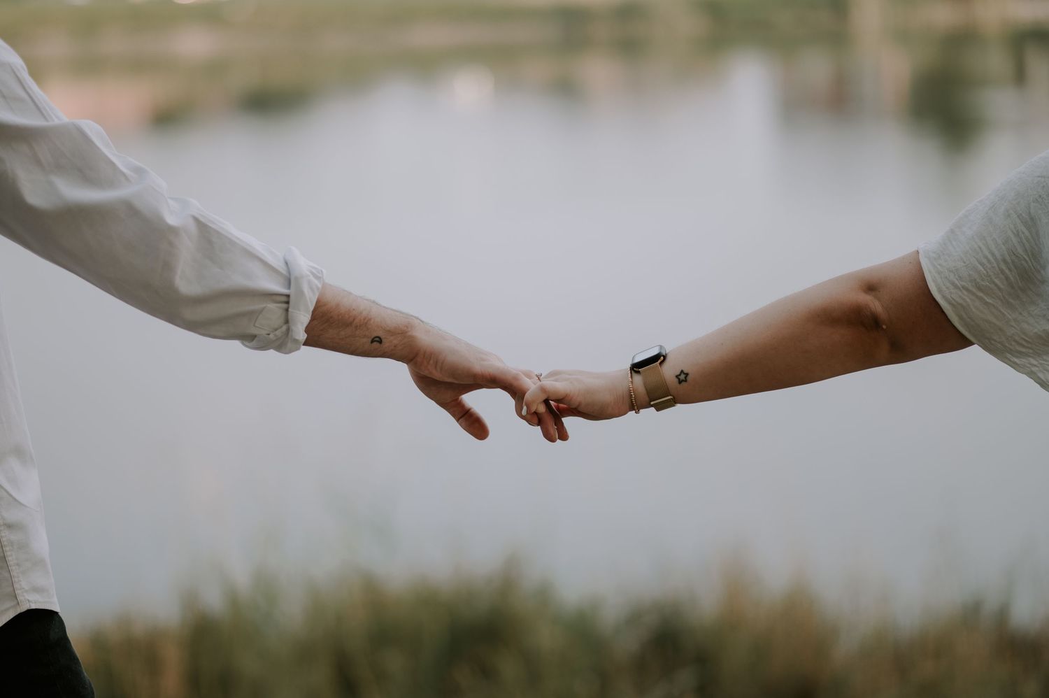 Two hands reaching towards each other with a serene lake in the background.