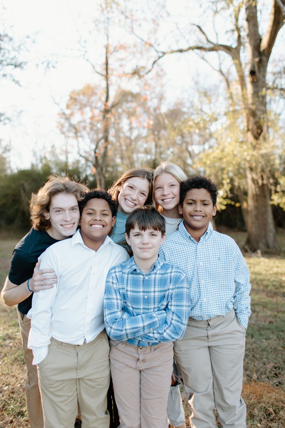 Children in coordinating blue and white outfits pose together outdoors in a natural setting.