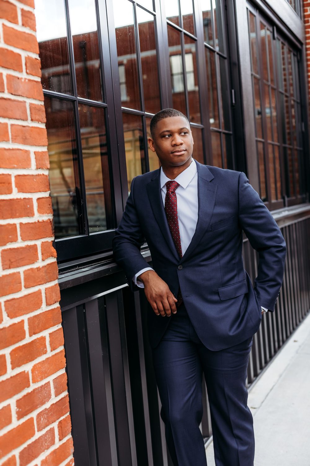 Professional wearing a navy suit and red tie poses against a brick wall with windows in an urban setting in North Haven, CT