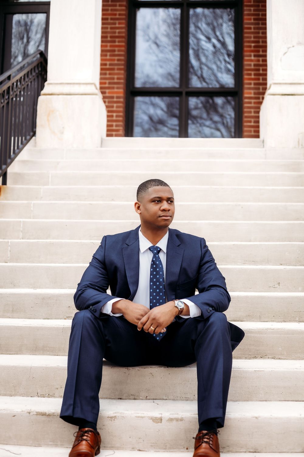 Professional portrait of someone in navy suit sitting on white stone steps of building North Haven, CT.
