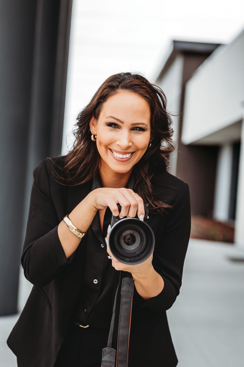 Person in black blazer smiles while holding photography equipment in outdoor setting in Hamden, CT.