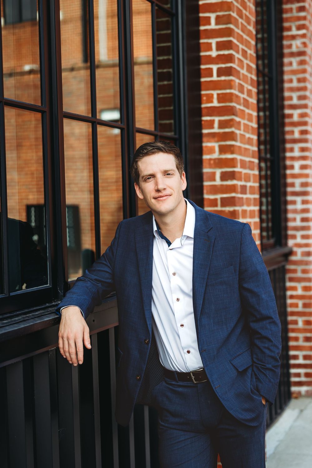 Professional portrait of someone in a navy suit and white shirt standing against a brick building with windows in Branford, CT.